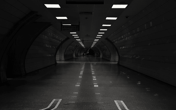 A picture of a road within a tunnel with symmetrical lighting on the top.