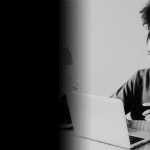 A woman sits at her laptop with a credit card in her hands.