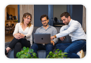 Three people sit comfortable on a couch and look at a laptop screen.