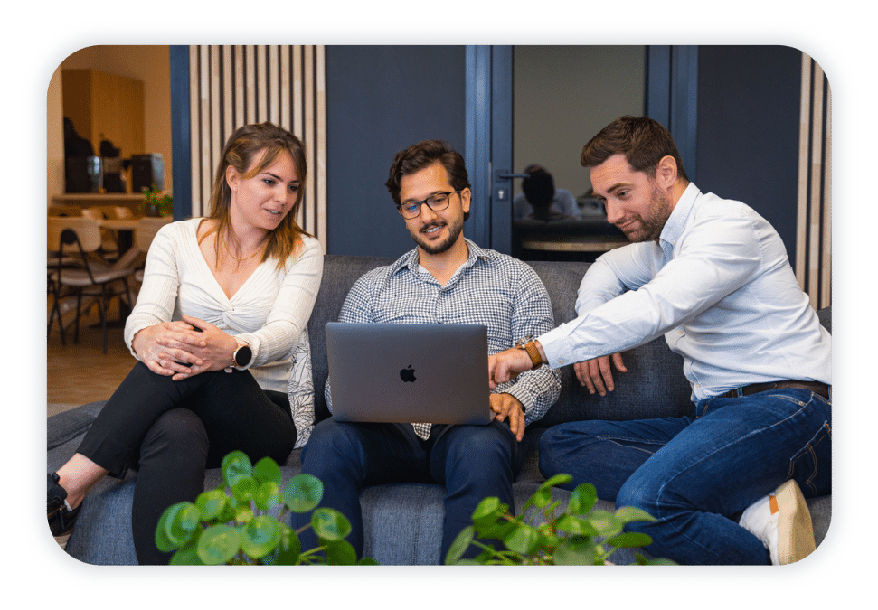 Three people sit comfortable on a couch and look at a laptop screen.