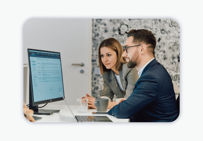 Two colleagues look at a desktop. 