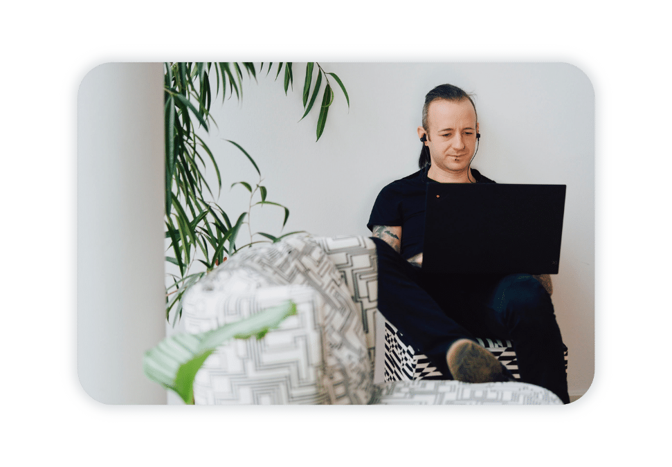 A man sits on a couch and works at his laptop. 