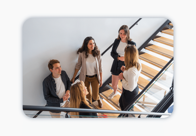 A group of people stand in a stairway having a chat.