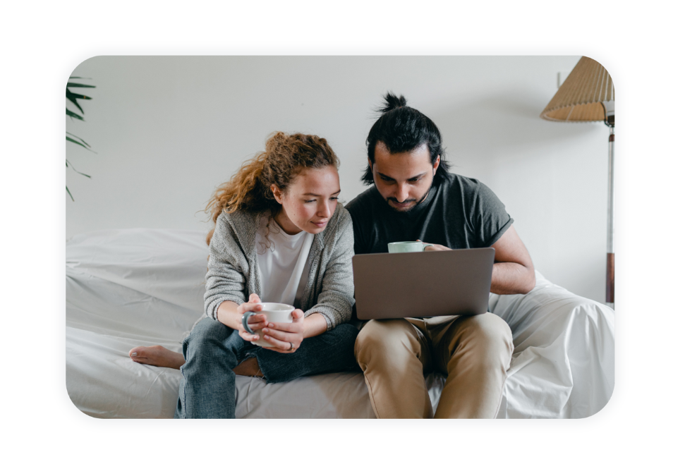 A couple sits on a couch and looks at their laptop