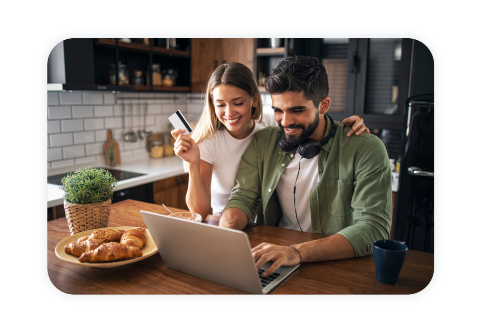 A couple is sitting in front of a laptop in their kitchen and is shopping online. 