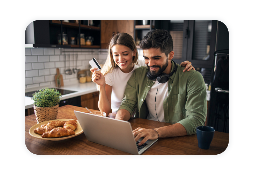 A couple is sitting in front of a laptop in their kitchen and is shopping online.